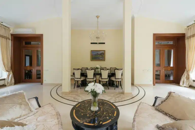Classic grand living room with circular marble floor, gilded lacquered table, dining room beyond and solid wood doors.