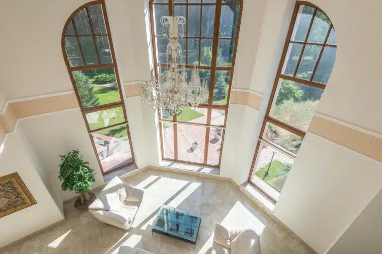 Manor house interior with double-height living room, large arched windows, crystal chandelier and garden view.