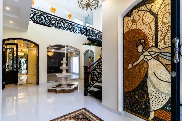Villa entrance hall with gold mosaic door panel, marble fountain, wrought iron staircase and double-height crystal chandelier.