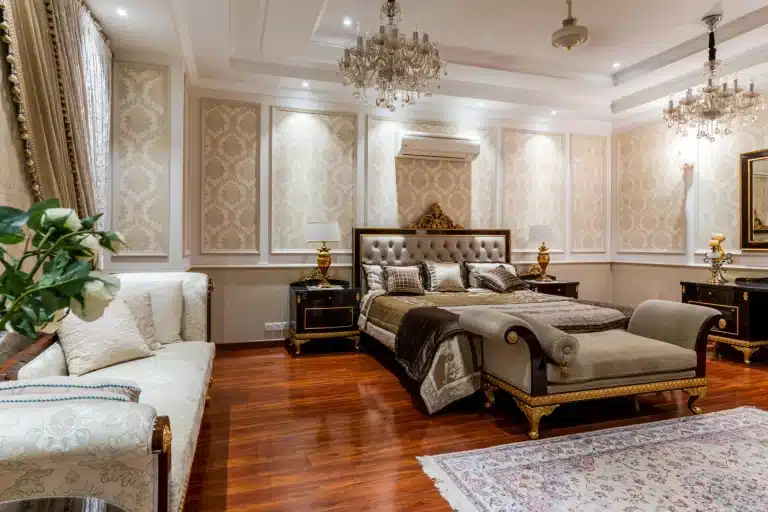 Baroque luxury bedroom with gold tufted headboard, damask wallpaper, crystal chandeliers and rich hardwood floor.