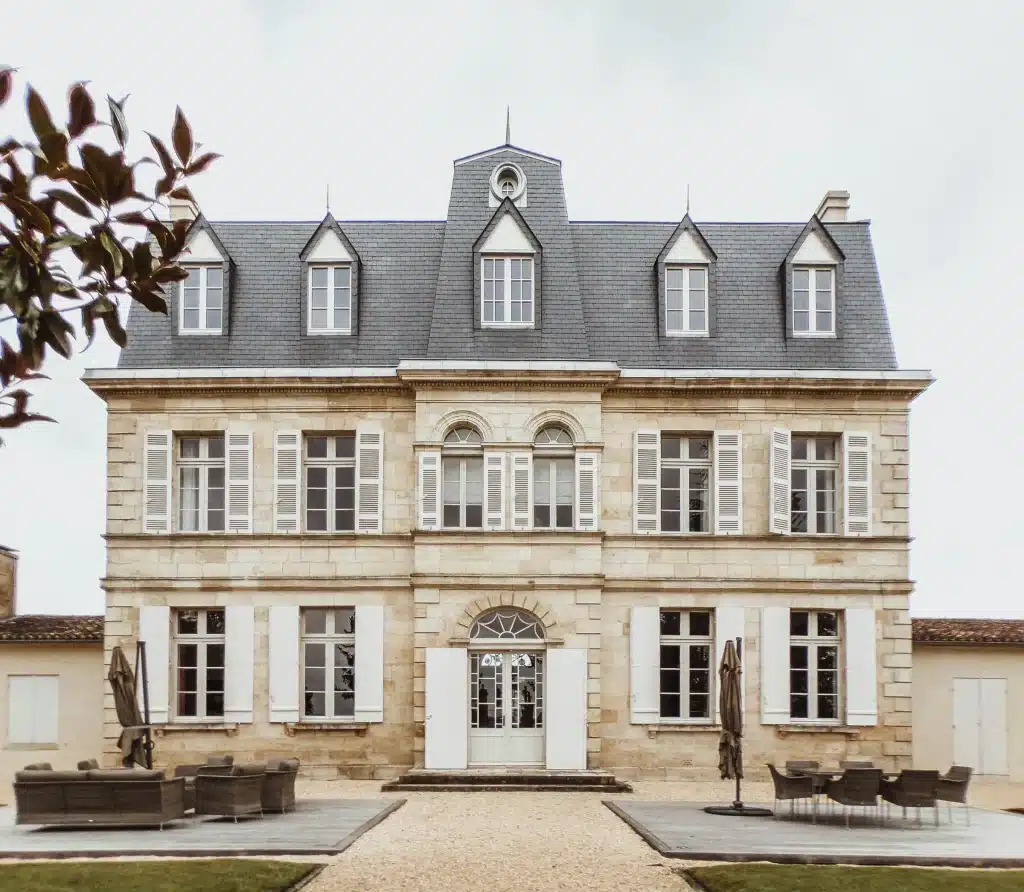 French manor house façade in cut stone with slate roof, dormer windows, white shutters and arched front entrance.